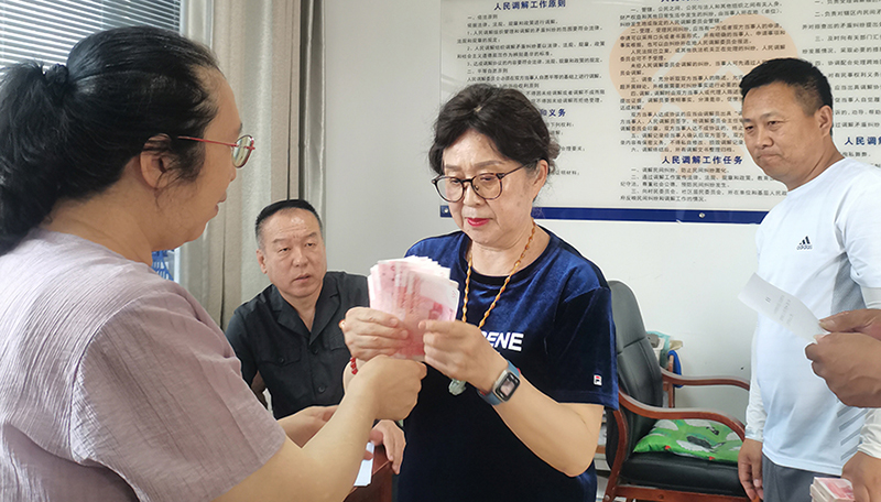 頭題片，5月30日，某藥業公司按協議約定完成第一期履行義務，將十萬現金交到法院，調解員付菊（左一）清點無誤之后交到農民工委托代理人徐某手中